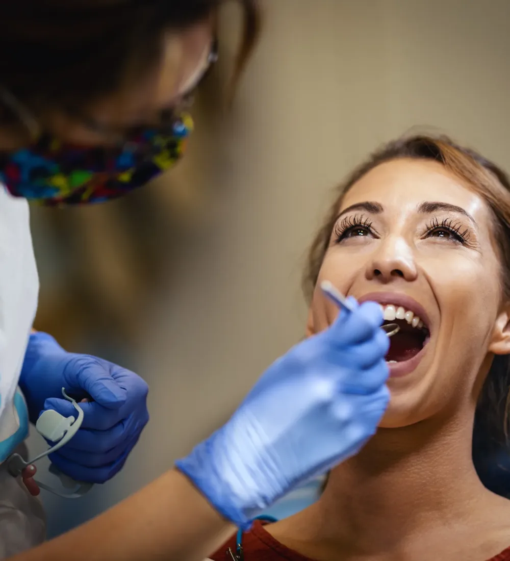 The beautiful young woman is at the dentist. She sits in the dentist's chair and the dentist checkup her teeth.